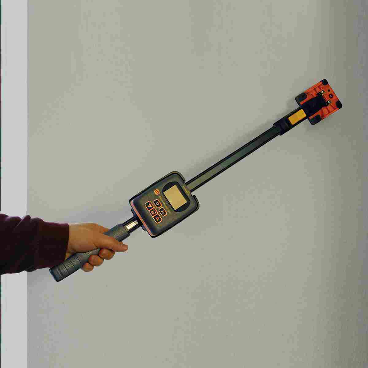 Hand hält den Protimeter Reachmaster Pro mit Sensorkopf an eine Wand.