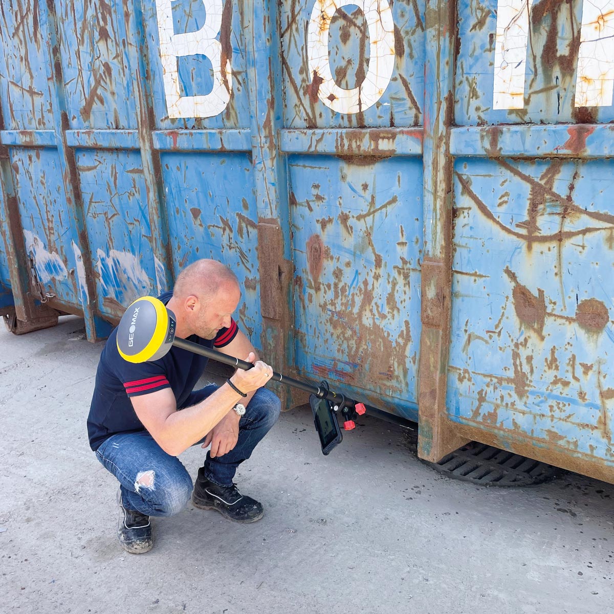 Vermesser misst mit stark geneigtem Lotstab und GeoMax Zenith60 unter einem Container.