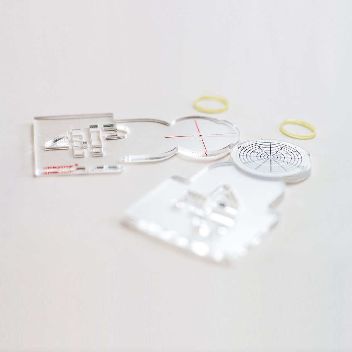 Rissmonitor SPEED Montageteile aus Acryl mit roten Zielmarken und gelben Gummibändern.
