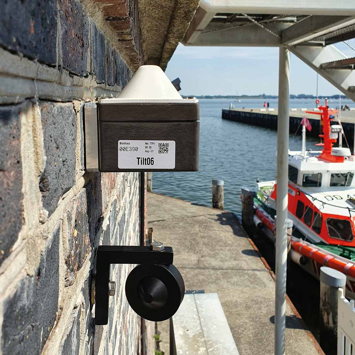 Senceive Flat Mesh 3 Repeater für drahtloses Monitoring, an einer Hafenmauer mit Blick aufs Wasser montiert.