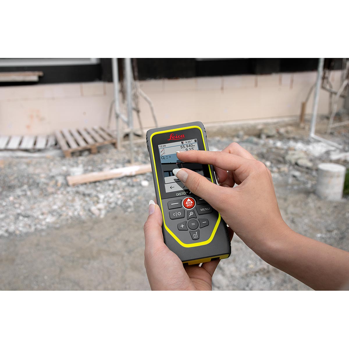 Hand bedient den Touchscreen des Leica Disto X6 auf einer Baustelle mit Gerüst.