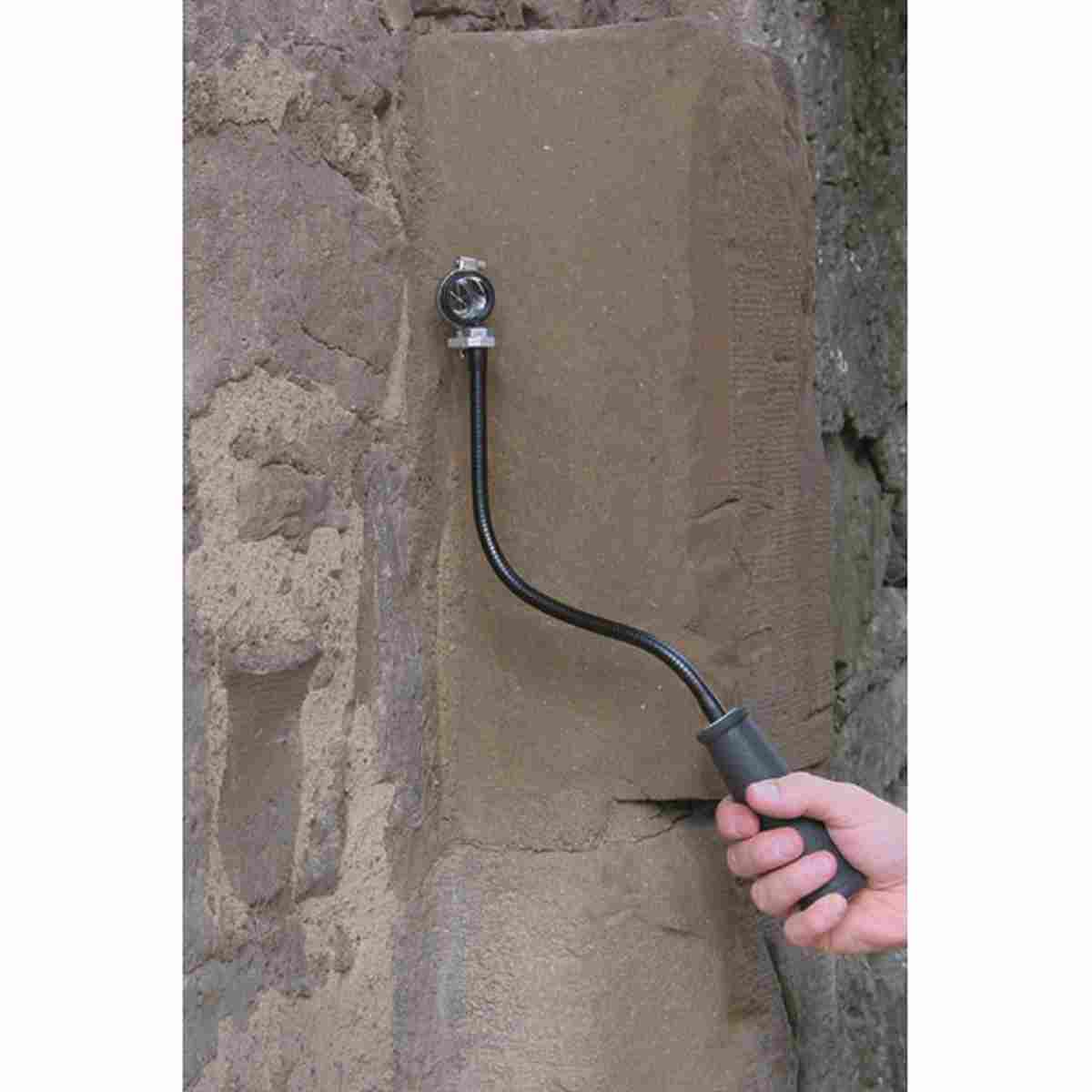 Hand hält den Schwanenhals mit Prisma an eine Natursteinmauer.