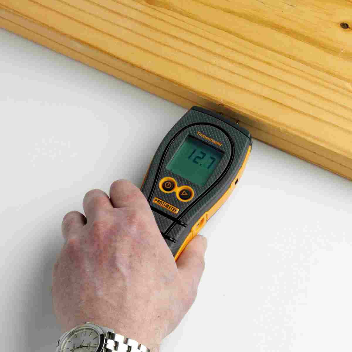 Eine Hand hält das Protimeter Timbermaster Feuchtigkeitsmessgerät an ein Holzbrett, um den Feuchtigkeitsgehalt zu prüfen.