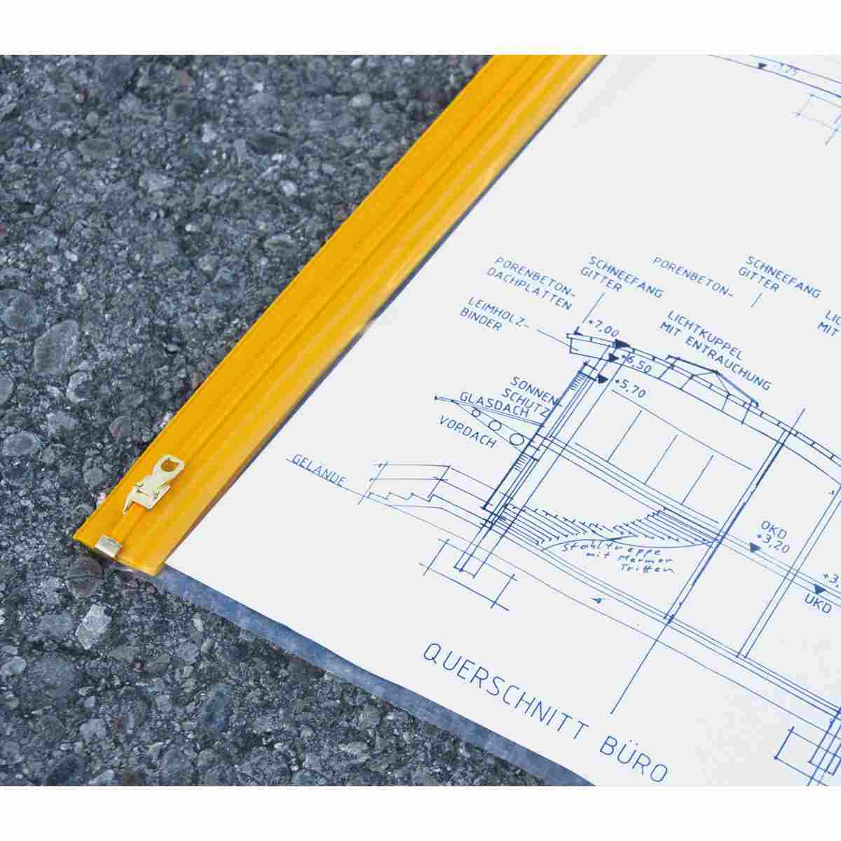 Planschutztasche mit gelbem Reißverschluss und eingelegtem Bauplan auf Asphalt.