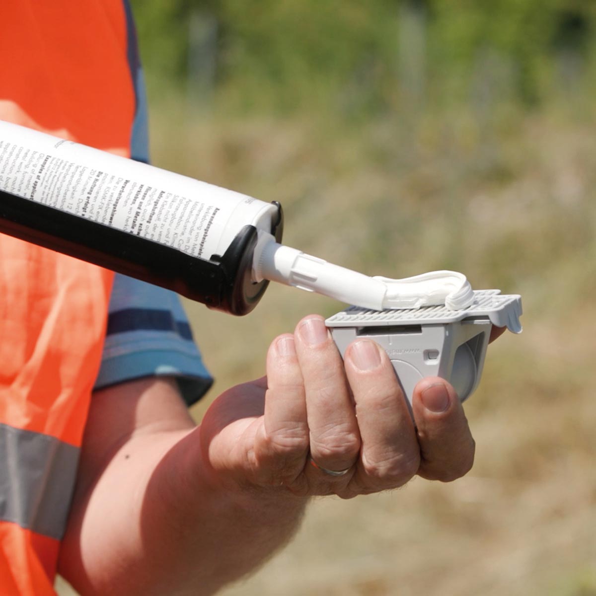 Montagekleber RSMK-FIX wird aus der Kartusche auf die Rückseite eines grauen Prismenhalters aufgetragen.