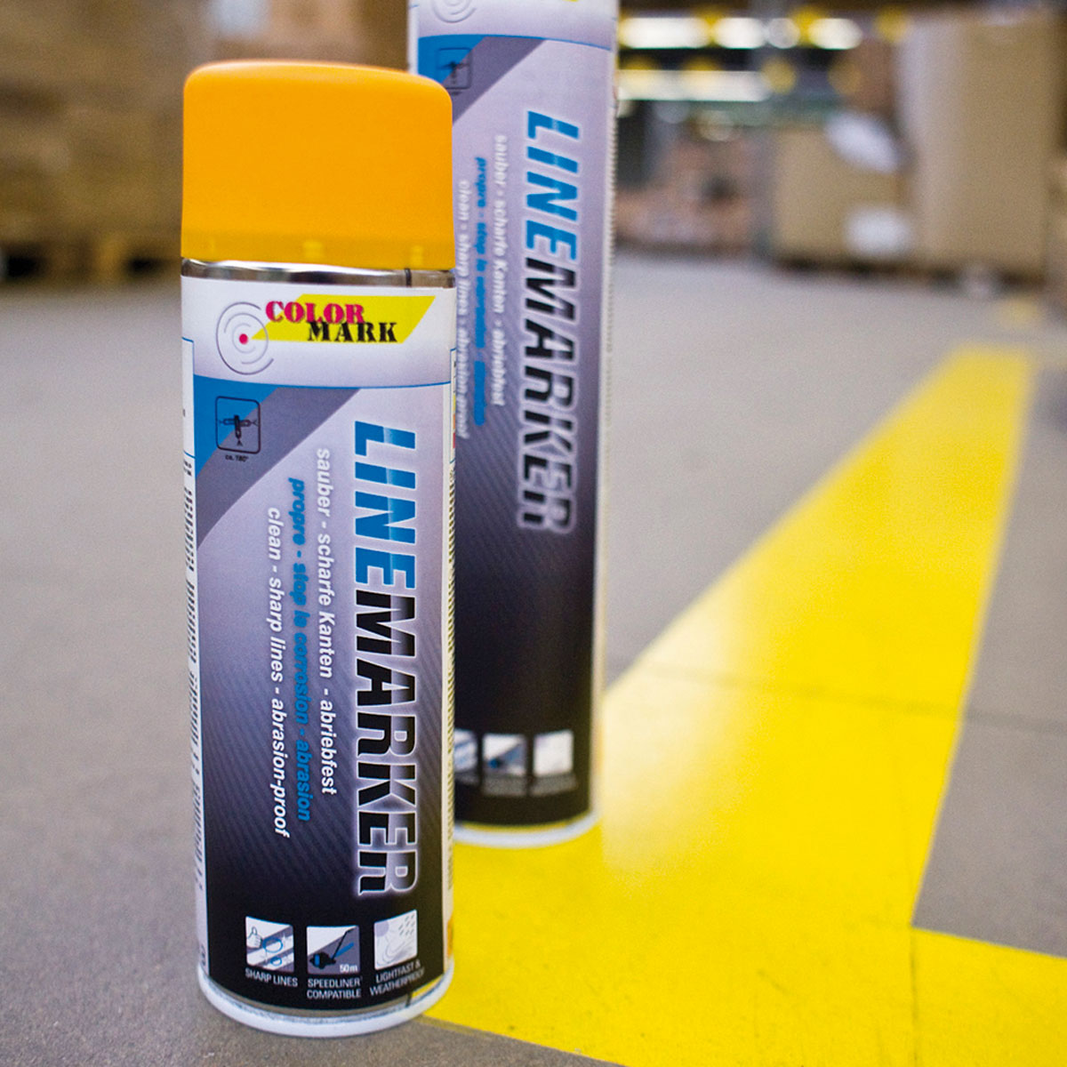 Zwei Colormark Linemarker Dosen mit gelber Kappe neben einer gelben Bodenmarkierung in einer Halle.
