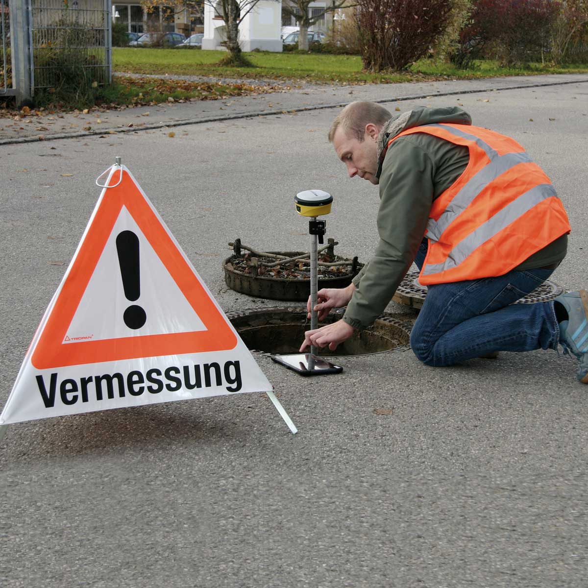 Vermesser in Warnweste misst mit dem proNIVO PNR21 einen Kanalschacht neben einem Warnschild Vermessung.