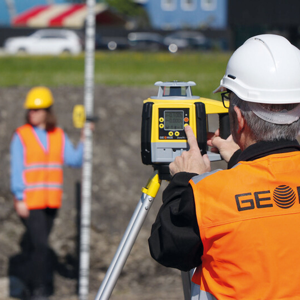Eine Fachkraft bedient den gelben GeoMax Neigungslaser im Außeneinsatz auf einer Baustelle.
