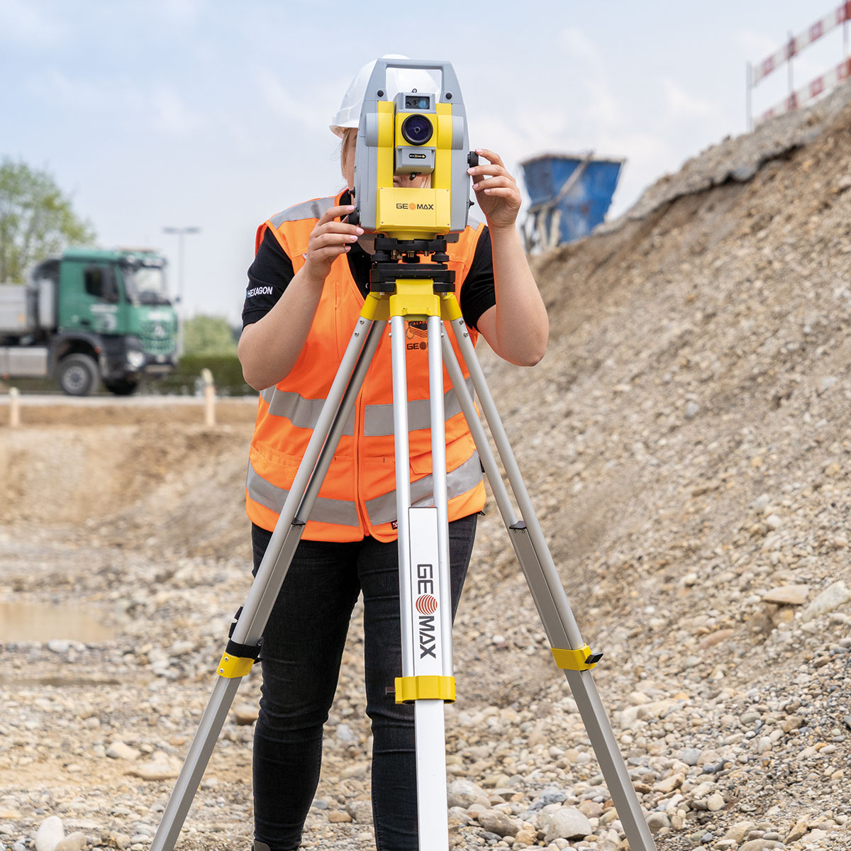 Vermesserin mit Helm und Warnweste blickt durch die GeoMax Zoom 95 auf einer Baustelle.