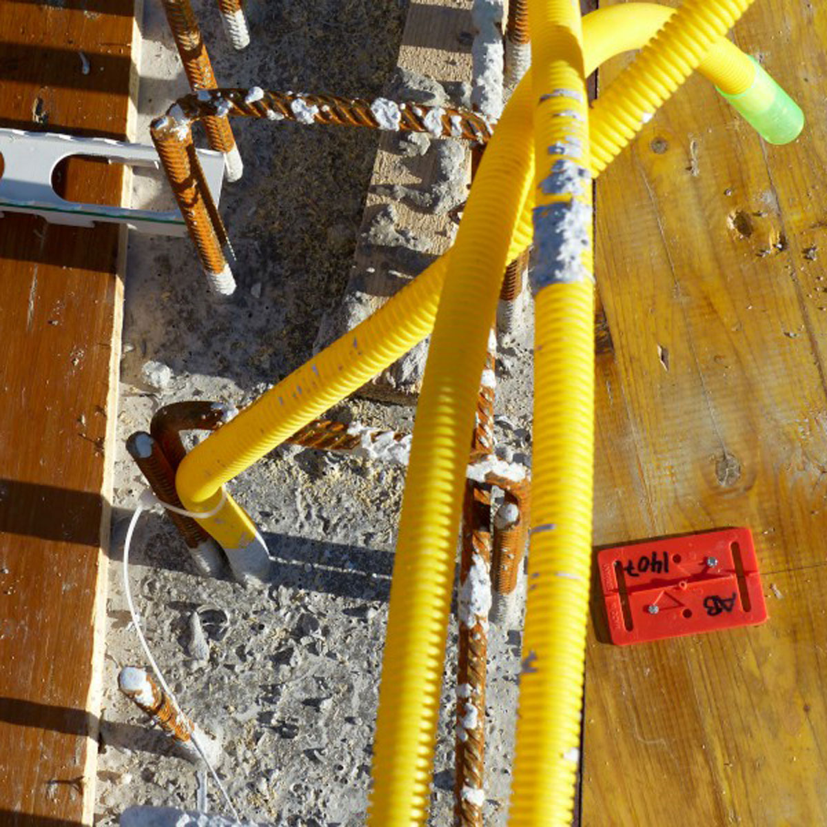 Beschriftete rote Meterriss-Plakette RS11 auf einer Holzschalung neben Bewehrungsstahl und gelben Leerrohren.