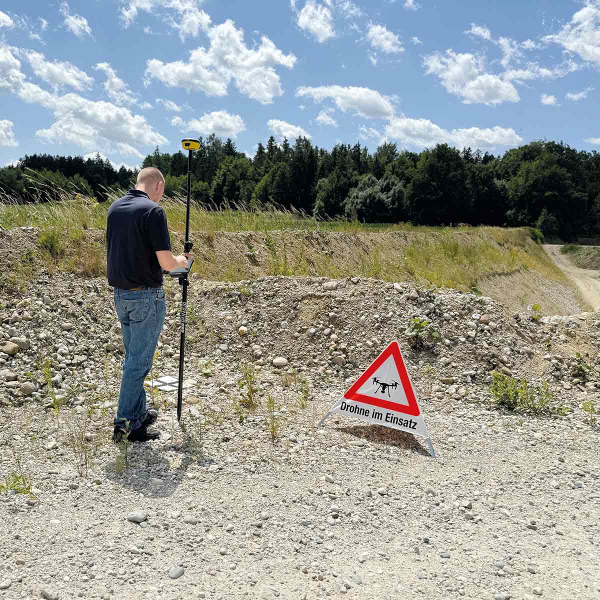 Vermesser mit GNSS-Rover in einer Kiesgrube neben dem Triopan-Faltsignal Drohne im Einsatz.