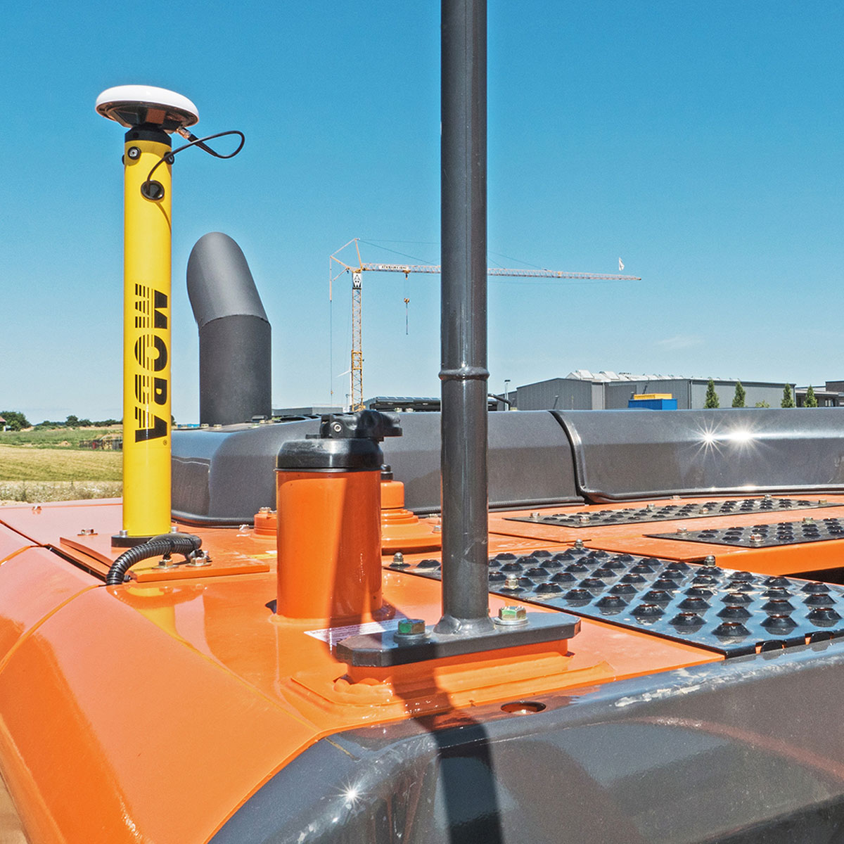 Gelber MOBA-Antennenmast mit GNSS-Antenne auf dem Heck eines orangen Baggers.