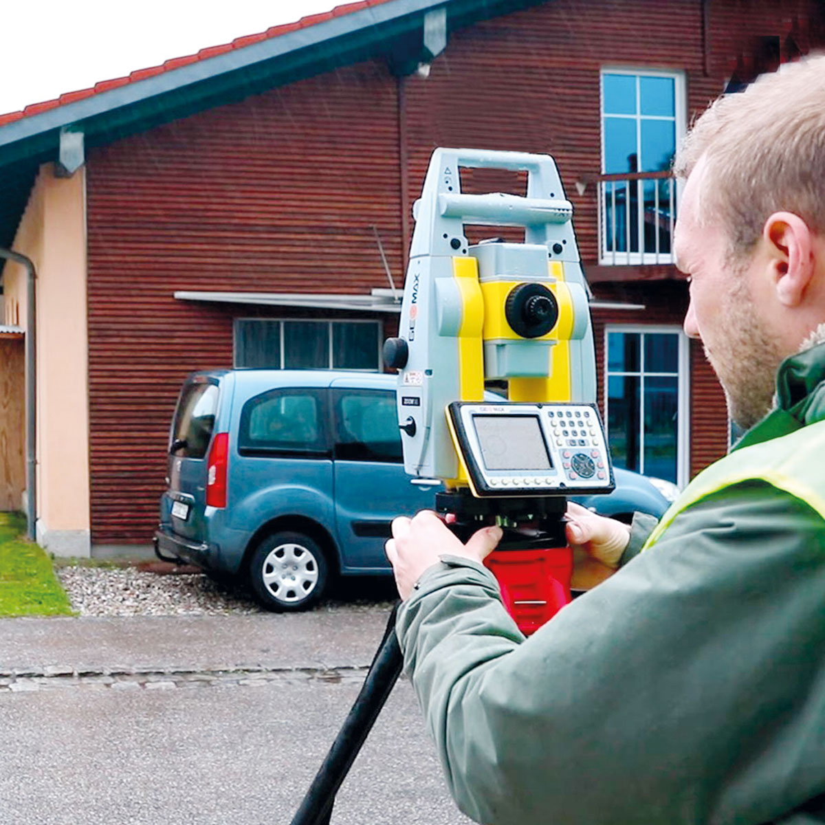 Vermesser richtet die GeoMax Totalstation Zoom 95 vor einem Wohnhaus mit Holzfassade aus.