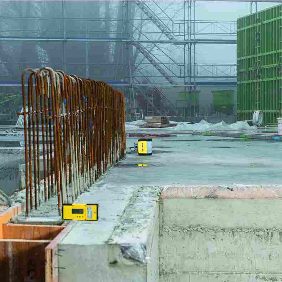 GeoMax Handempfänger auf einer Betonwand auf der Baustelle, im Hintergrund ein Rotationslaser.