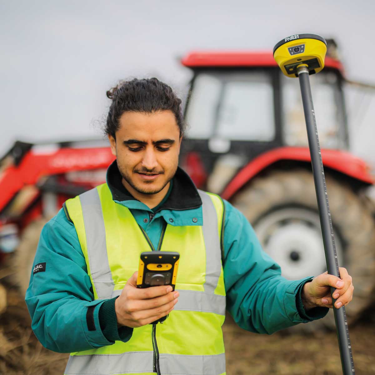 Mann in Warnweste mit Feldrechner und proNIVO PNR21 am Lotstab vor einem roten Traktor.