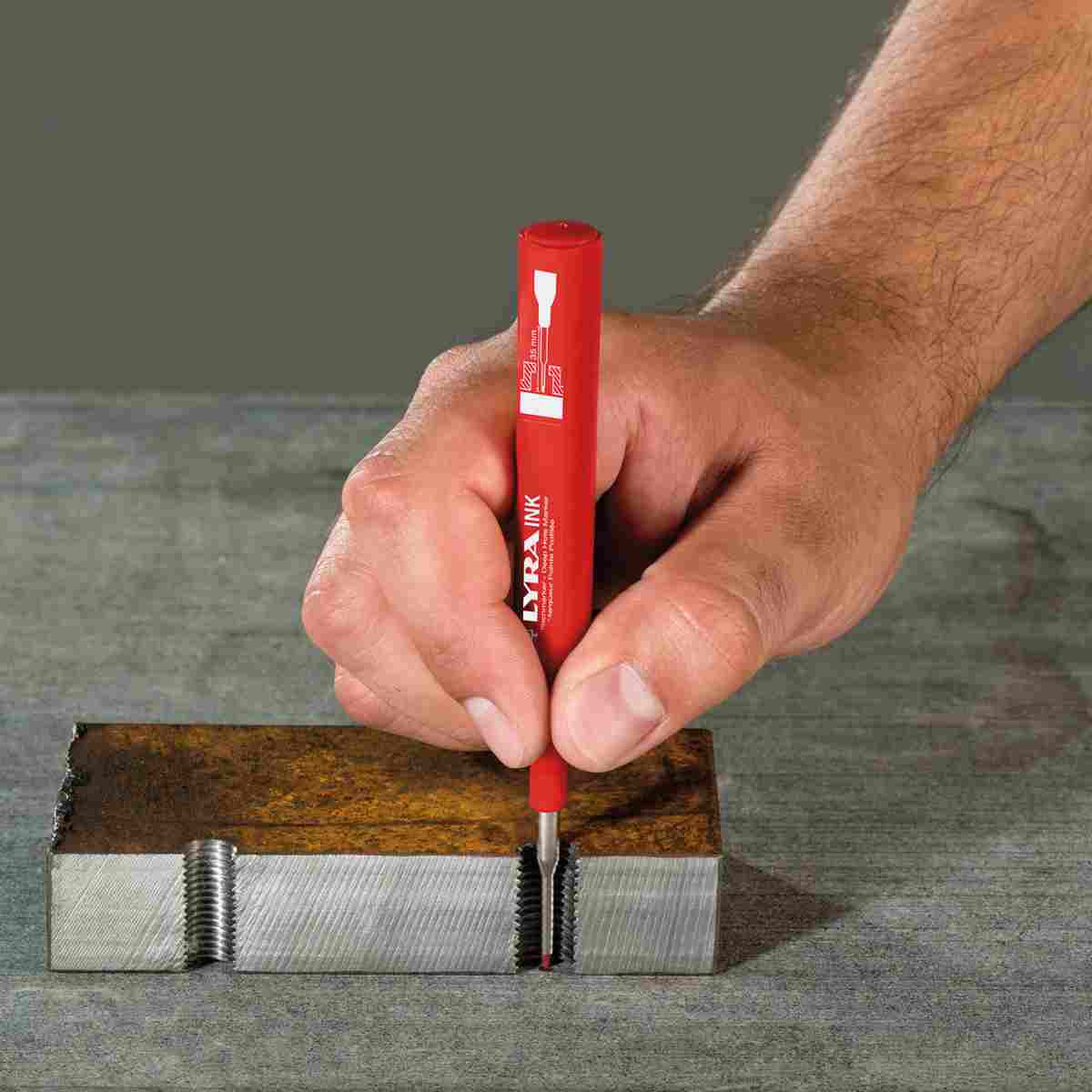 Hand markiert mit einem roten Tieflochmarker die Gewindebohrung in einem Metallblock.