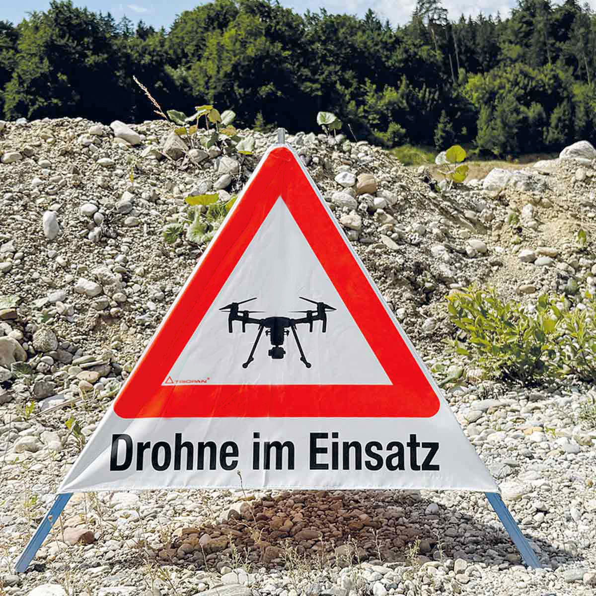 Triopan-Faltsignal mit Drohnensymbol und Aufschrift Drohne im Einsatz auf einem Kieshaufen.