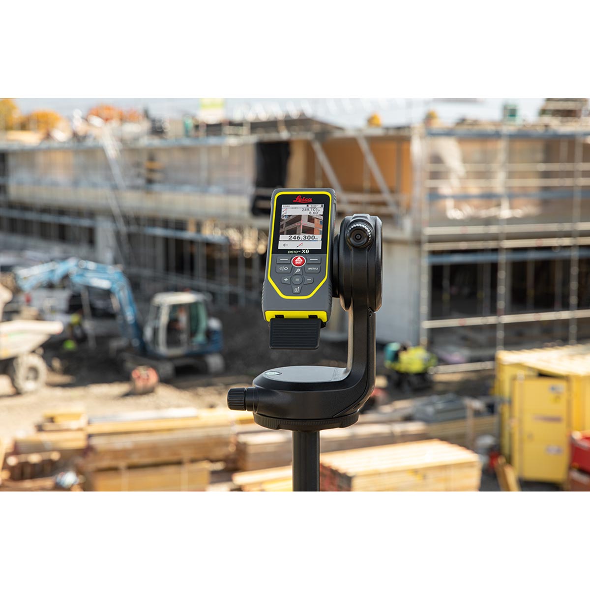 Leica Disto X6 auf dem DST 360 Adapter vor einer Großbaustelle mit Bagger und Rohbau.