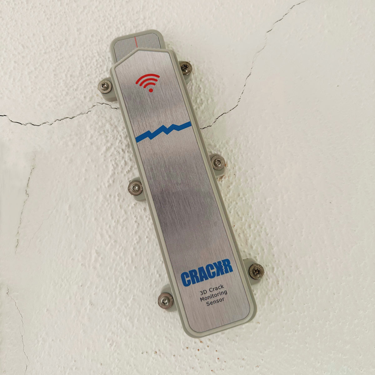Nahaufnahme des CrackR 3D Rissmonitors, montiert auf einer weißen, leicht rissigen Wandoberfläche.