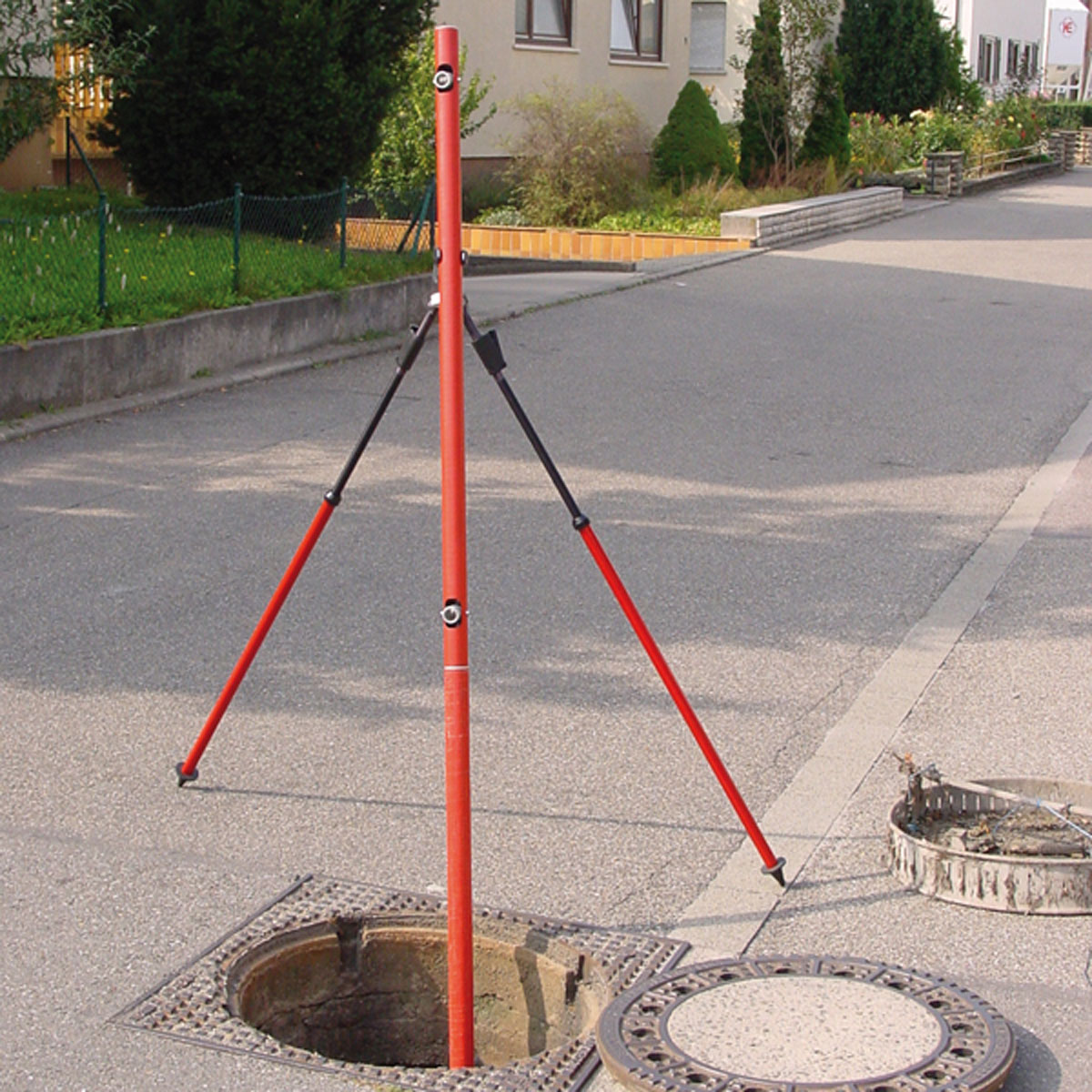 Roter Kanalmessstab mit Vektor-Zweibeinstativ über einem geöffneten Kanalschacht auf der Straße.