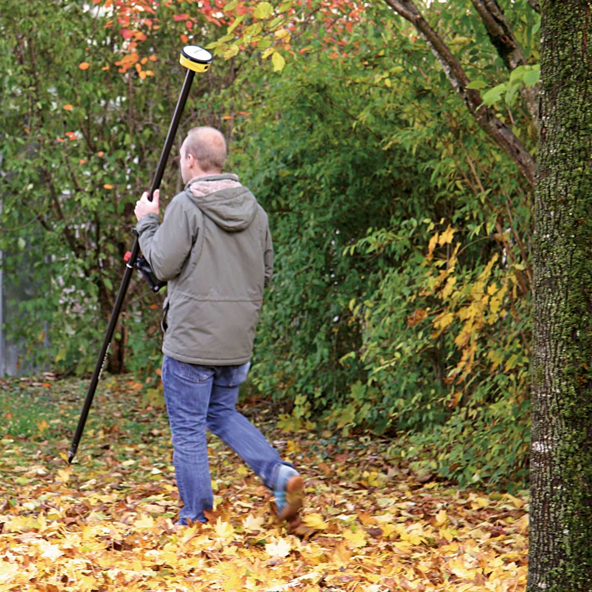 Mann trägt einen Lotstab mit proNIVO PNR21 durch herbstliches Laub zwischen Büschen.