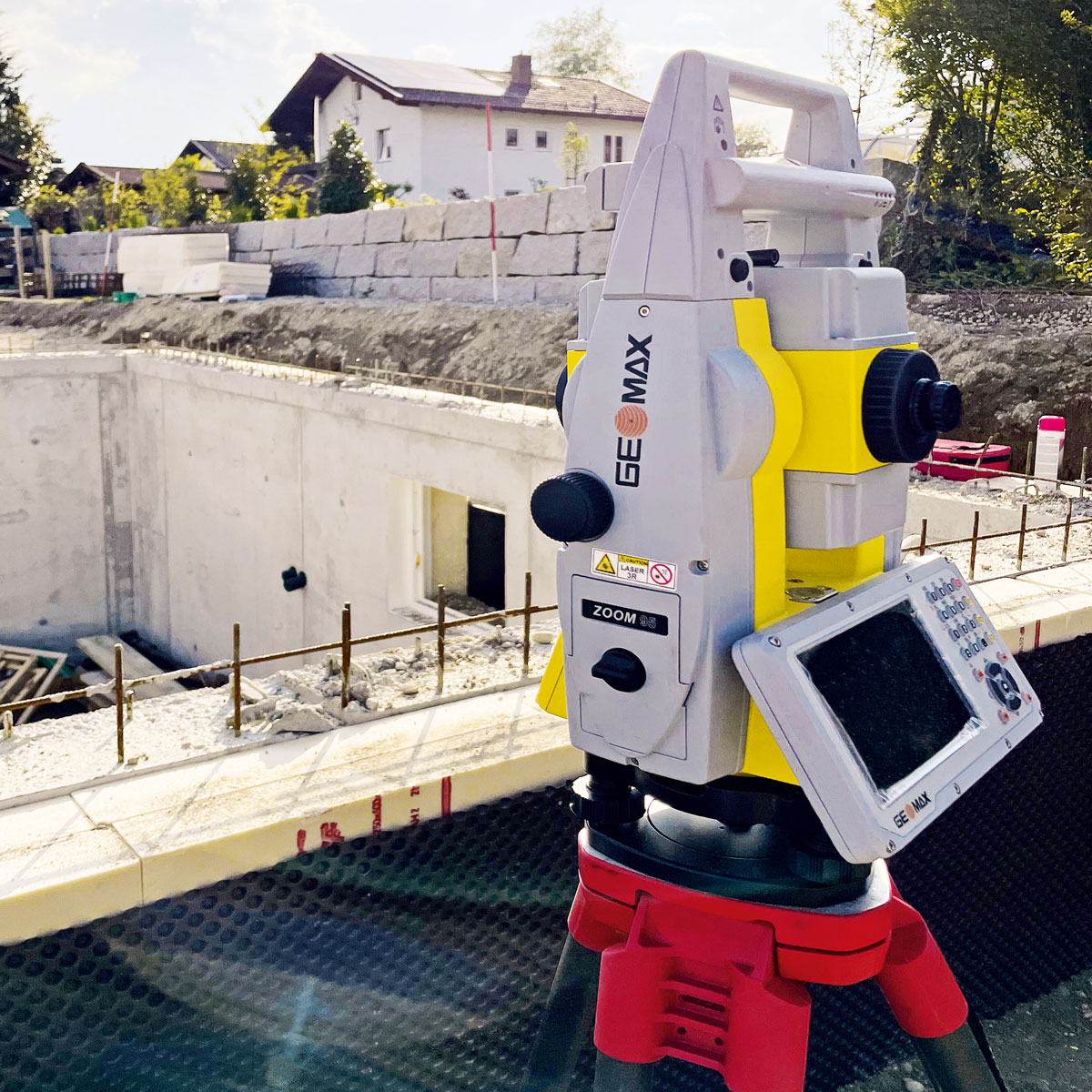 GeoMax Totalstation Zoom 95 auf rotem Stativ vor einer Baugrube mit Betonwänden.
