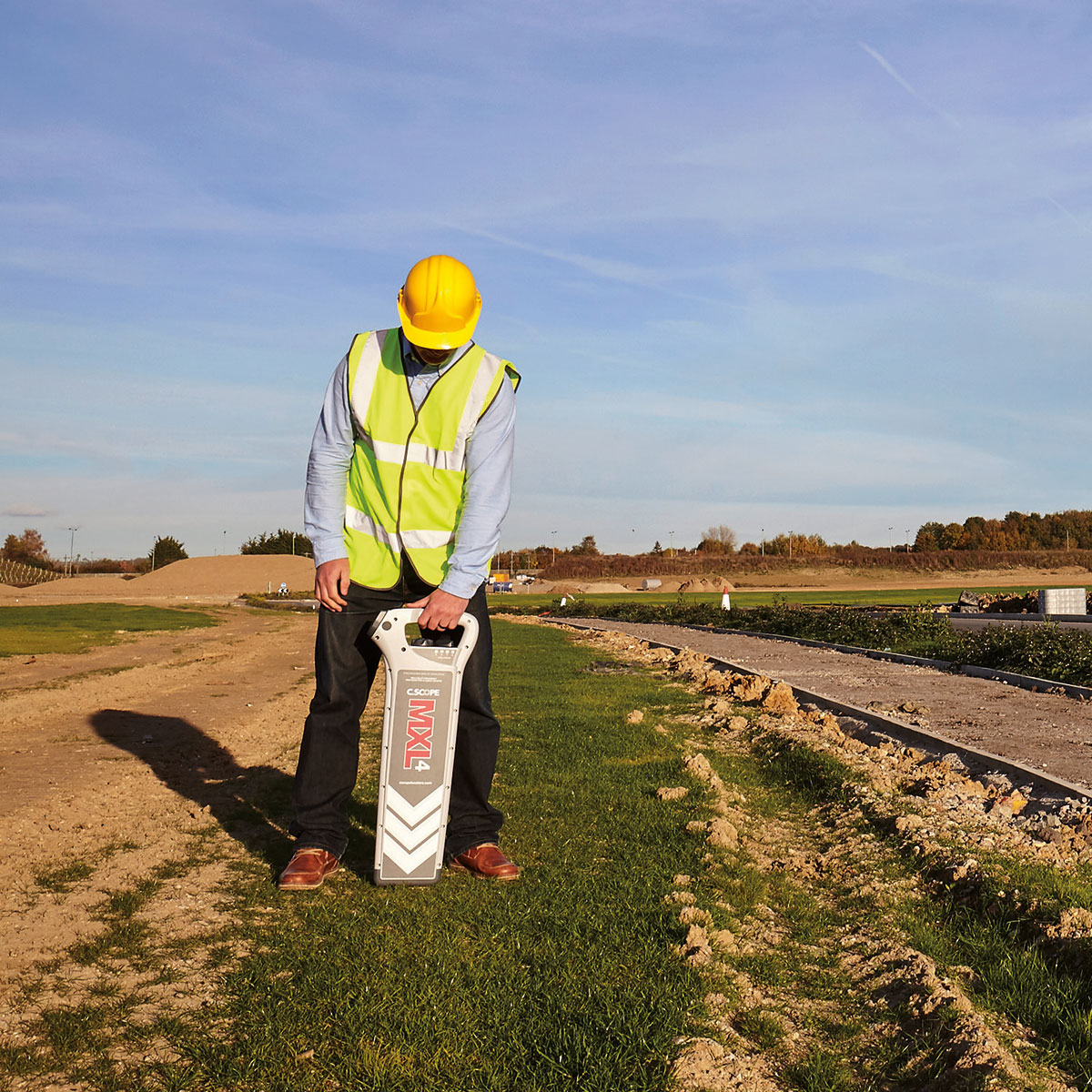Mitarbeiter mit Helm und Warnweste sucht mit dem C.Scope Kabelsuchgerät MXL4 auf einer Baustelle Leitungen.